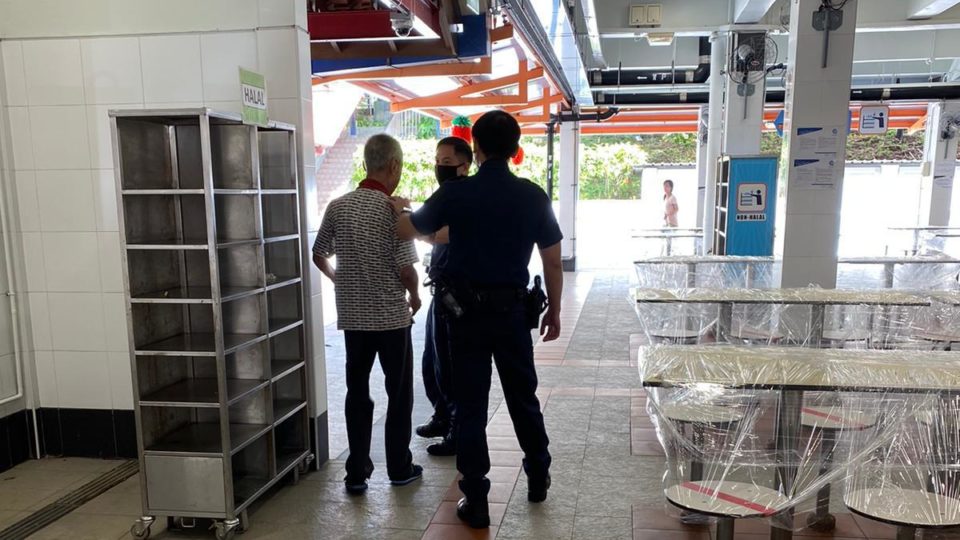 Two police officers confront an elderly man at a hawker center in a photo dated April 9, 2020. Photo: Masagos Zulkifli/Facebook