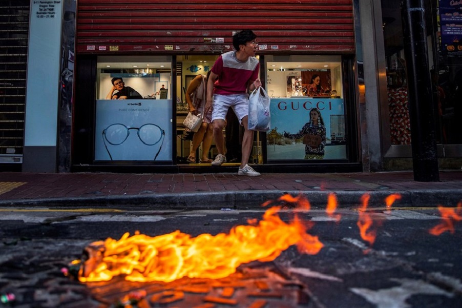 Customers cautiously exit an eyeglass store past a burning molotov cocktail as demonstrators clash with police on Nov. 2, 2019. Photo: Tyrone Siu/Reuters