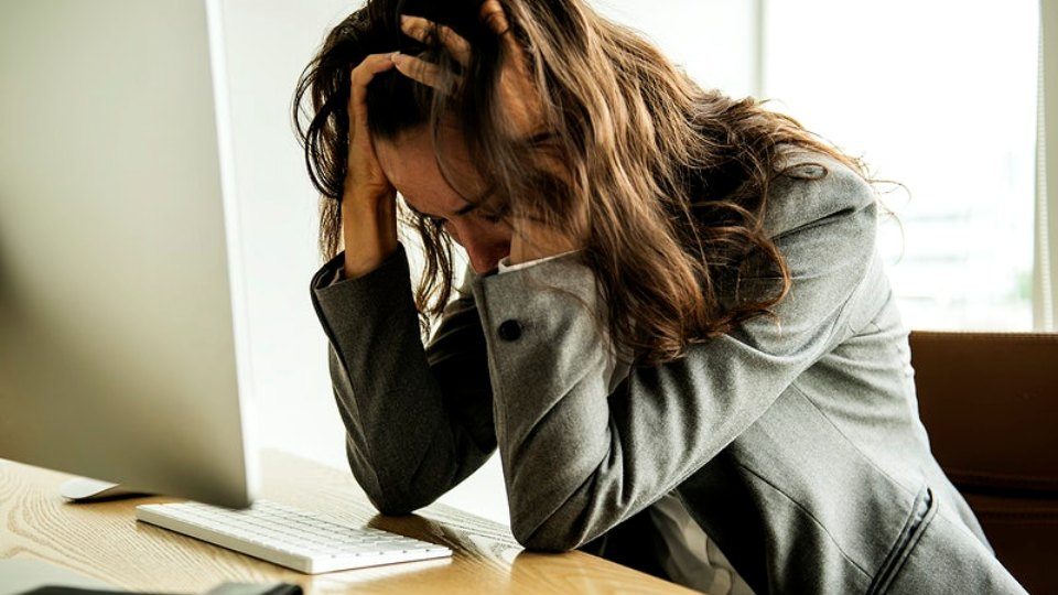 A woman sits in front of a computer with head in her hands. Photo: RawPixel
