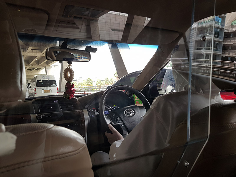 Bangkok reflected in the protective barrier, on the other side of which a PPE-clad driver took me from airport to hotel. 