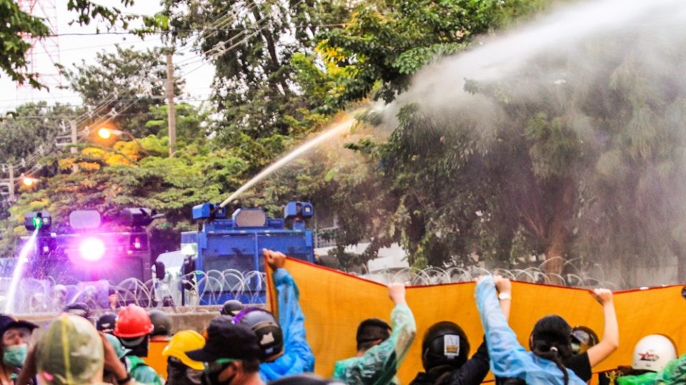 Protesters on Tuesday raise a mat to protect themselves from chemical water cannons shot by riot police on Samsen Road. Photo: Coconuts
