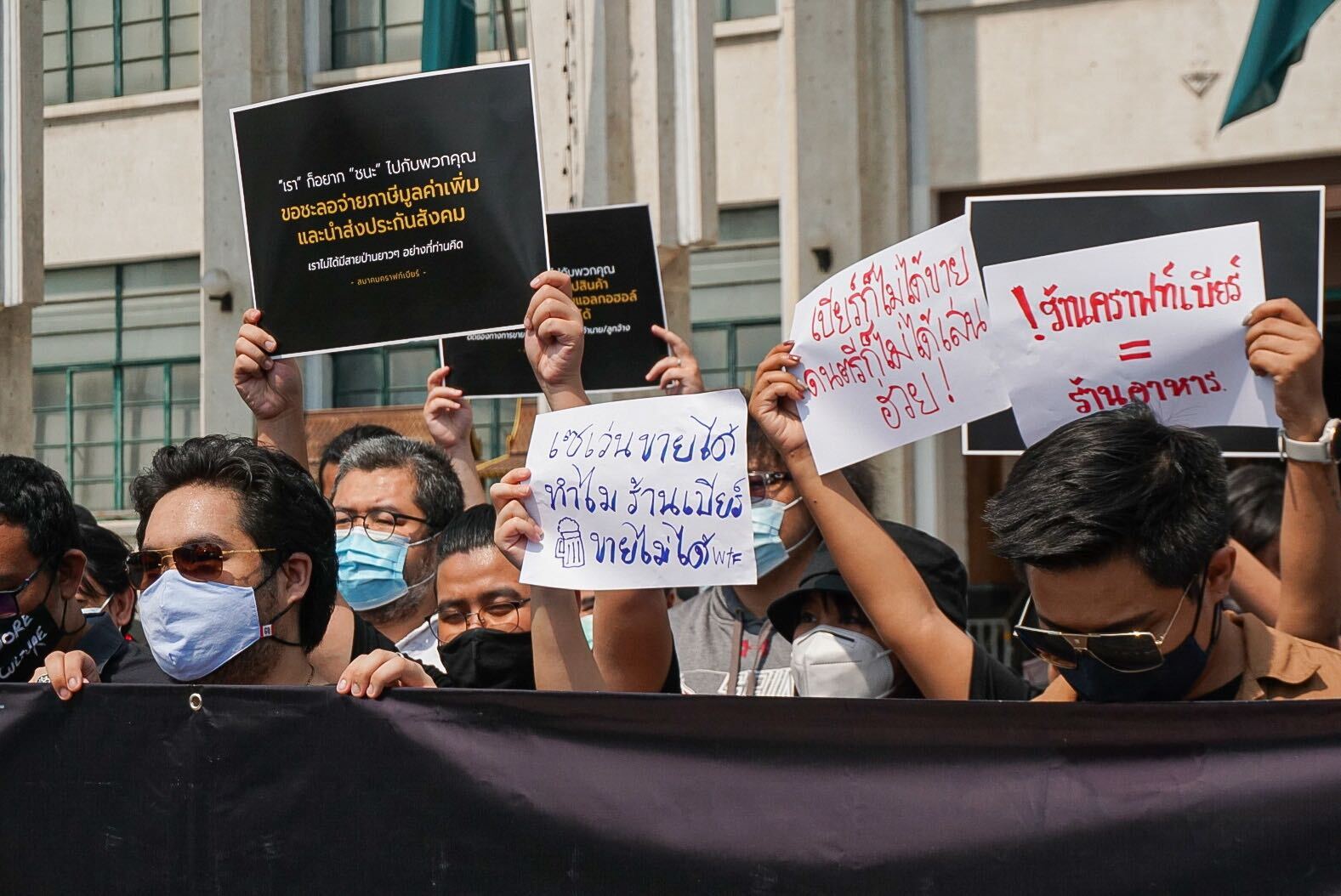 “Why can 7-Eleven be open 24 hours, but bars not at all?” reads a banner held this afternoon by members of the Craft Beer Association outside City Hall.