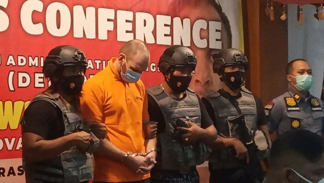 Andrei Kovalenka stood in between law enforcers during a press conference in Denpasar on March 23, 2021. Photo: Istimewa via Kumparan