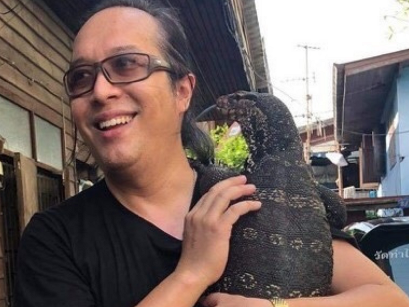 A photo file of Jitkamol Thanasal holding a monitor lizard.