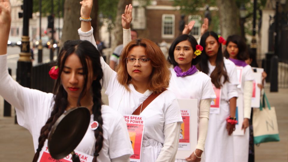 Women, wearing red lipstick and flowers, hold on three finger salute in London to protest against Myanmar military regime on June 19th, birthday of State Counselor Aung San Suu Kyi and International Day of the Elimination of Sexual Violence in Conflict. (Twitter)