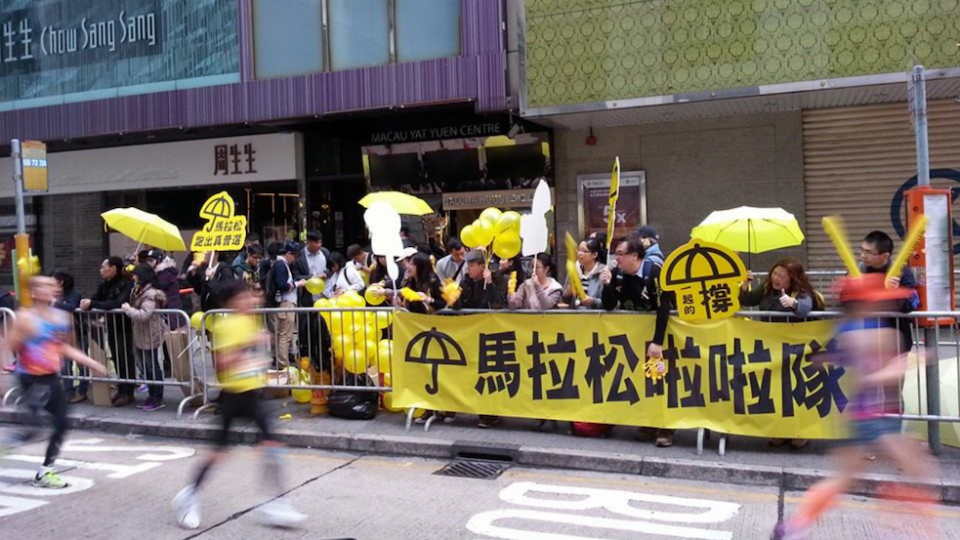 Supporters with yellow umbrellas and a sign reading “marathon cheerleading squad” cheer on runners at the 2015 Standard Chartered Hong Kong Marathon. Photo: Facebook/Pete Chong