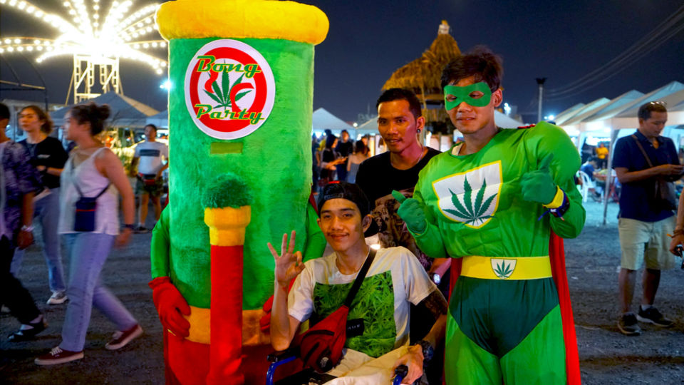 A young man in a wheelchair poses with a human bong mascot and Super Weedman in April, 2019, at the Runway 3119 Night Market in Bangkok. Photo: Teirra Kamolvattanavith / Coconuts Bangkok