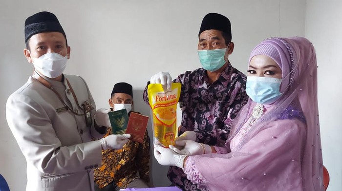 Newlywed couple Supadi (2nd from right) and Sumariati (right) holding up his cooking oil dowry. Photo: KUA Sooko