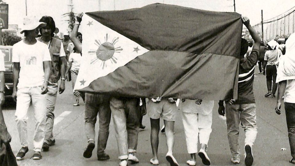 A group of protesters carries the Philippines flag during the People Power Revolution. Image: Presidential Museum and Library PH (2010-2016)