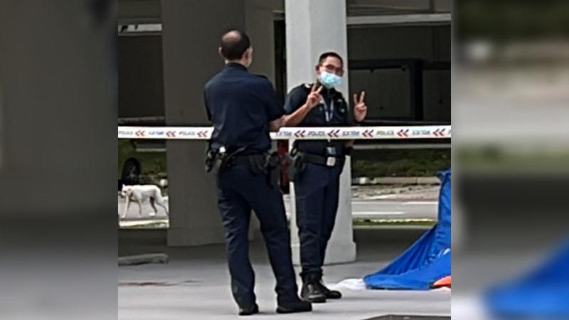 A police officer posing with a ‘V’ sign next to a dead body at a crime site. Photo: Tracy Lim/Facebook
