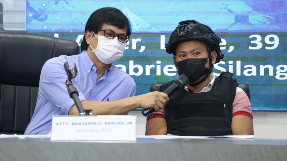 Interior Interior Secretary Benjamin Abalos Jr. (left) interviews Joel Estorial, the alleged killer of Philippine radio broadcaster Percival Mabasa following Estorial’s surrender to police, Oct. 18, 2022. Photo: Department of the Interior and Local Government handout