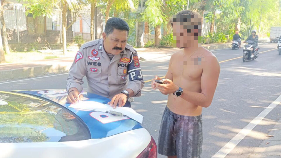 Police ticketing a shirtless motorcyclist for not wearing a helmet. Photo: Handout by Bali Police