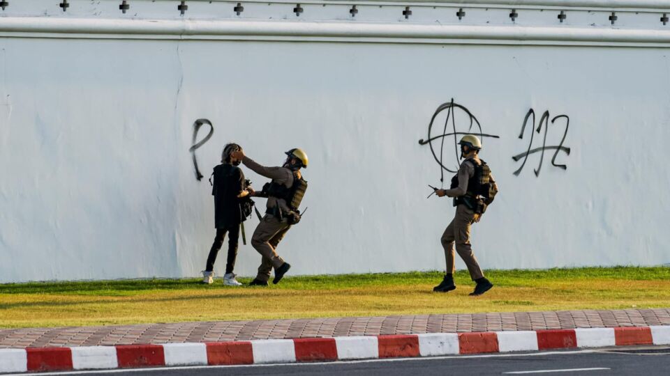 Police officers approach a man who writes on a wall of the Grand Palace on Tuesday. Photo: Egg Cat Cheese / Facebook