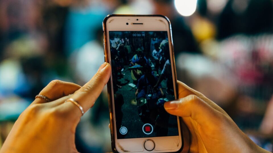 A person holding up a phone to record. Photo: Unsplash
