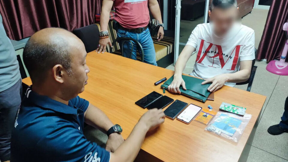 Pakphoom “New” Saengnil, seated in white, on Sunday night at the Khlong Luek Police Station located just across the border from Cambodia. Photo: Khlong Luek Police Station