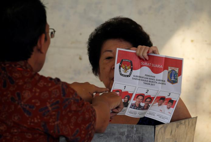 An election official assists an ethnic Chinese Indonesian woman before she casts her ballot during an election for Jakarta’s governor on February 15, 2017. Photo: REUTERS/Beawiharta