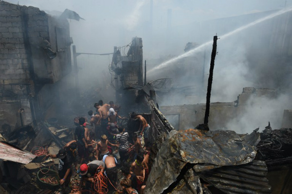 Residents jostle for position as they scavenge for recyclable materials to be sold later, amidst smoke and smouldering debris after a fire hit an informal settlers area near a container port in Manila on May 9, 2017. Local media reported a teenage boy died and 30 houses were burnt in the incident. PHOTO: Ted Aljibe, AFP